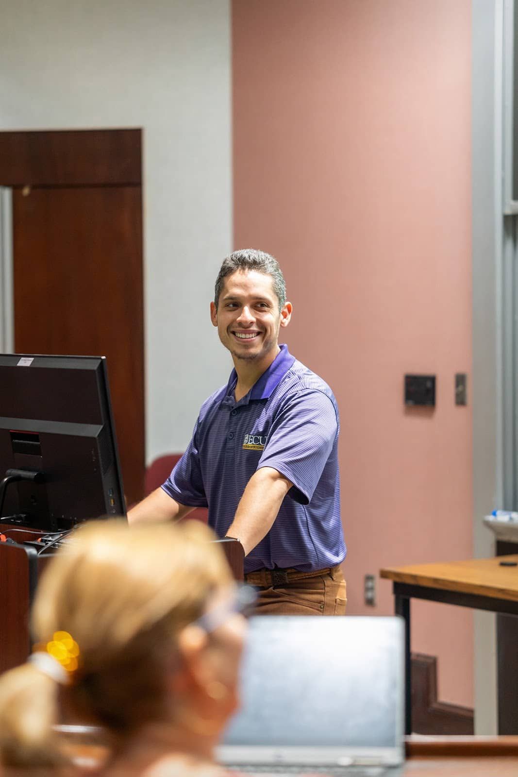 College professor smiling at students while standing at podium.