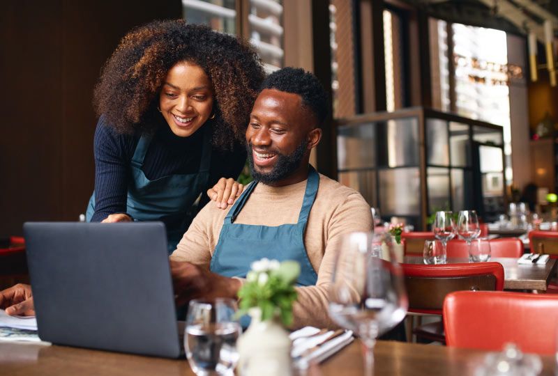 Restaurant owners smiling and working on laptop
